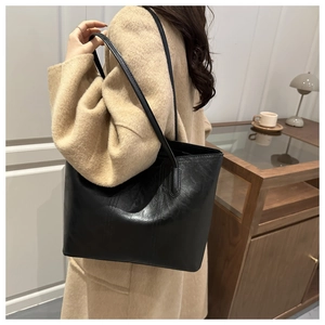 Large black faux leather tote bag with vertical stitching shown on model with tan coat