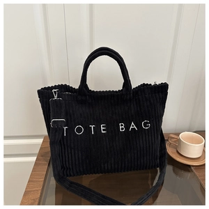 Detail of black corduroy tote bag showing embroidered text and adjustable shoulder strap