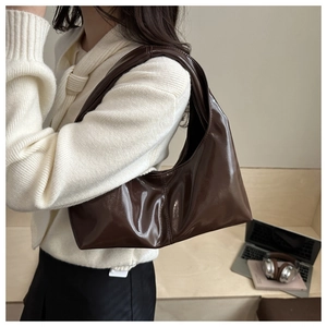 Detail of dark brown glossy patent leather tote bag styled on model in modern office