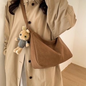 Brown suede large tote bag with plush charm and vertical stitching on beige coat