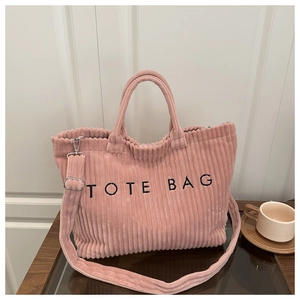Pink corduroy tote bag with embroidered logo on a wooden table in a cozy indoor setting