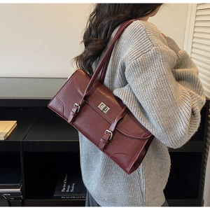 Détail du sac sous le bras en cuir bordeaux avec boucle argentée sur pull en maille