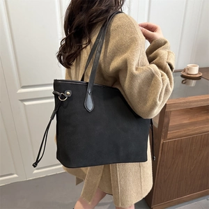 Minimalist black suede tote bag with drawstring detail shown on a model in a cozy interior