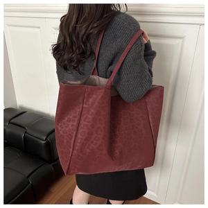 Detailed view of burgundy leopard print leather tote bag worn on a shoulder