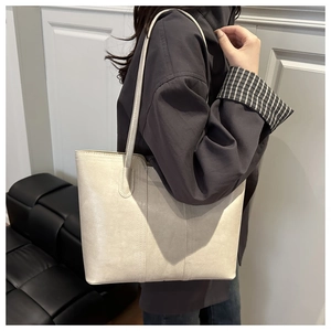 Chic beige tote bag on a model's shoulder against a minimalist white wall backdrop