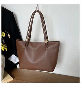 Détail d'un grand sac fourre-tout marron avec boucles dorées accroché au mur blanc