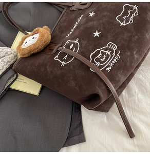 Detail of coffee brown faux suede tote bag featuring cat embroidery and plush pendant