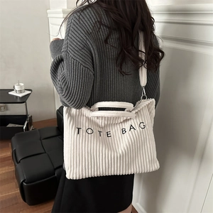 White corduroy tote bag with black embroidery and shoulder strap worn by a model
