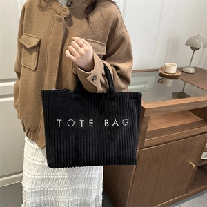 Minimalist black corduroy tote bag with embroidered logo shown in a lifestyle scene