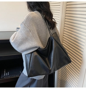 Detailed view of black large-capacity tote bag in textured faux leather on shoulder