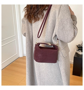 Deep burgundy leather tote bag with gold buckle worn as a crossbody on a minimalist model