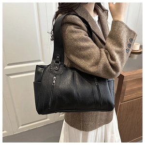 Detail view of a black leather tote bag with vertical zippers and shoulder strap