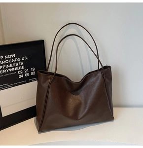 Detailed view of a dark brown large tote bag with textured faux leather on a white stand