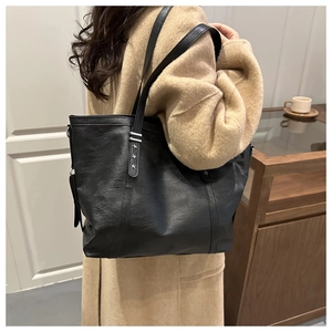 Close-up of black leather tote bag with three metallic star rivets on the shoulder strap