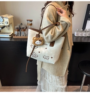 Close-up of a white tote bag featuring cartoon animal prints and a plush bear charm