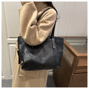 Large black minimalist tote bag with star rivets worn over a camel wool coat
