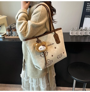 Close-up of canvas tote bag with cat graphics, brown leather trim and plush bear charm