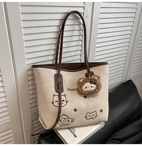 Close-up of cream tote bag with cat print, star patterns, and brown plush bear pendant