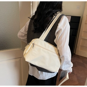 Minimalist beige nylon tote bag with front zipper pocket shown on a model's shoulder