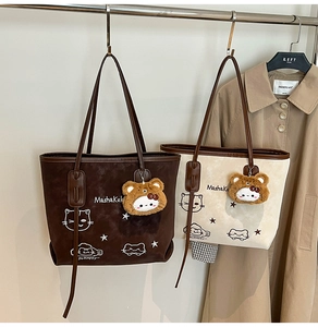 Detail of suede tote bag featuring cartoon embroidery and a plush bear head charm