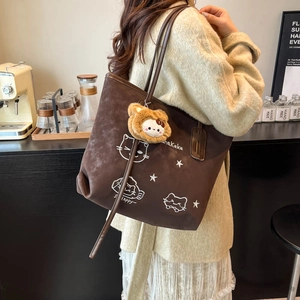 Brown suede tote bag with cartoon cat embroidery and plush charm in a cafe setting