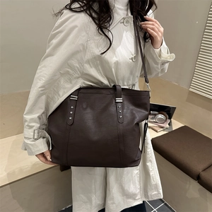 Minimalist large brown leather tote bag with star rivets shown on a shoulder