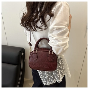 Detail of burgundy vintage textured handbag with embossed COIH'2DN brand logo and strap