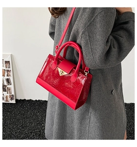 Detail of red embossed leather handbag with gold V-shaped metal lock and sleek handle