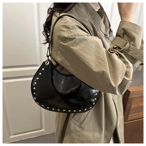 Fashionable black crescent hobo bag with gold rivets worn over a stylish trench coat