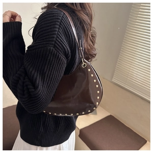 Detail of dark brown dumpling bag with rivets and glossy patent leather finish