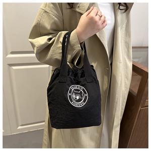 Détail du sac seau en nylon noir imperméable avec cordon et logo sur un manteau beige