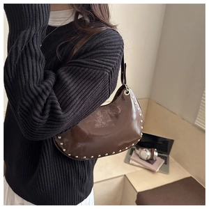 Detail view of dark brown crescent bag with gold studs on a glossy leather surface