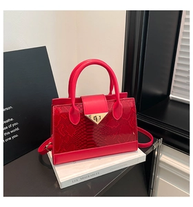 Detail shot of a red textured handbag with a gold triangular metal buckle and snakeskin pattern