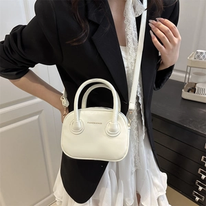 Minimalist white mini crossbody bag with double handles shown on a model in a suit