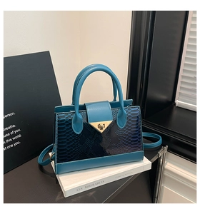 Detail of teal leather handbag with snake pattern texture and gold triangle metal lock