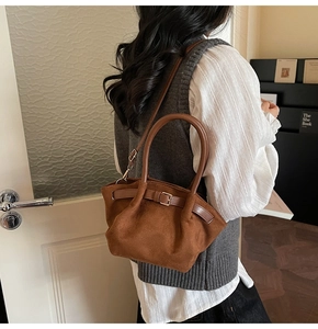 Brown matte suede handbag with buckle detail styled on a model in a minimalist setting