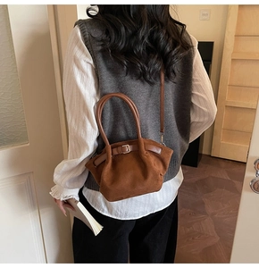 Detail of a brown matte crossbody bag featuring a belt buckle and round handles on a model
