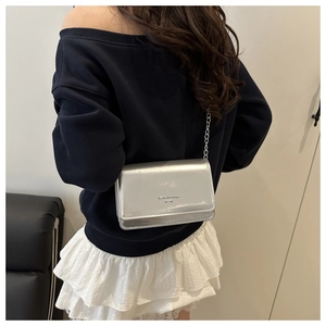 Detail van de zilveren metallic crossbody tas met ketting gedragen door een model