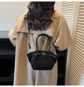 Detail of black matte handbag with decorative strap and textured handle worn with trench coat