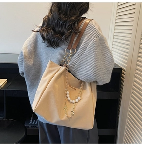 Detail of beige tote bag with gold chain strap, large pearls and clover pendant