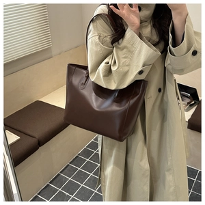 Detail of a large caramel brown leather tote bag paired with an elegant beige trench coat