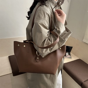 Brown leather tote bag with gold stud detail shown worn by a model in a cozy indoor setting