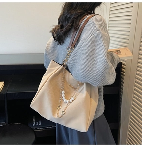 Detail of beige large tote bag with decorative pearl chain and brown leather strap