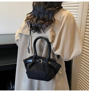 Detail of a black matte handbag with dual top handles and decorative buckle on a model