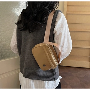 Détail d'un sac bandoulière en nylon kaki avec sangle rose porté à l'épaule, vue arrière