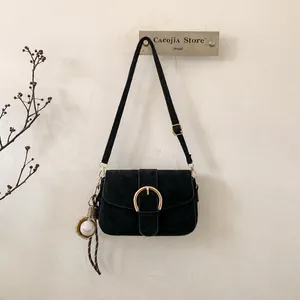 Detail of black suede shoulder bag featuring a large gold horseshoe buckle and baseball charm