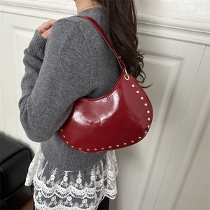 Deep red crescent underarm bag with gold studs and glossy finish shown on model