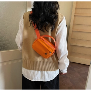 Détail d'un sac bandoulière orange vif avec un accent métallique rond sur le devant