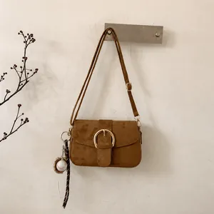 Detail of dark brown suede crossbody bag with gold buckle and baseball charm