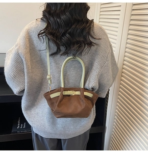 Detail of a brown suede crossbody bag with sage green handles shown on a model
